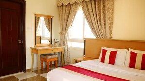 Una habitación de hotel con piso a cuadros, un escritorio de madera con una silla, una cama con ropa de cama roja y blanca, y un espejo grande en la pared.
