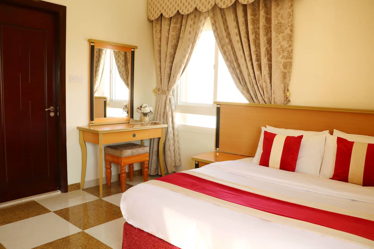 A hotel room with a checkered floor, a wooden desk with a chair, a bed with red and white bedding, and a large mirror on the wall.