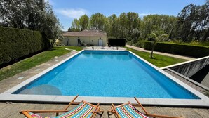 A rectangular swimming pool with two wooden lounge chairs with striped cushions in the foreground. - Casa Aguas Mansas (Cantanhede)