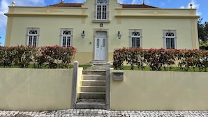 A two-story building with a symmetrical facade, a central entrance with a door, and a small staircase leading up to it. - Casa Aguas Mansas (Cantanhede)