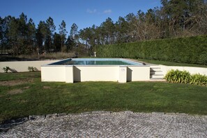 Una piscina rectangular con solárium empedrado, rodeada de un césped cuidado y un seto.