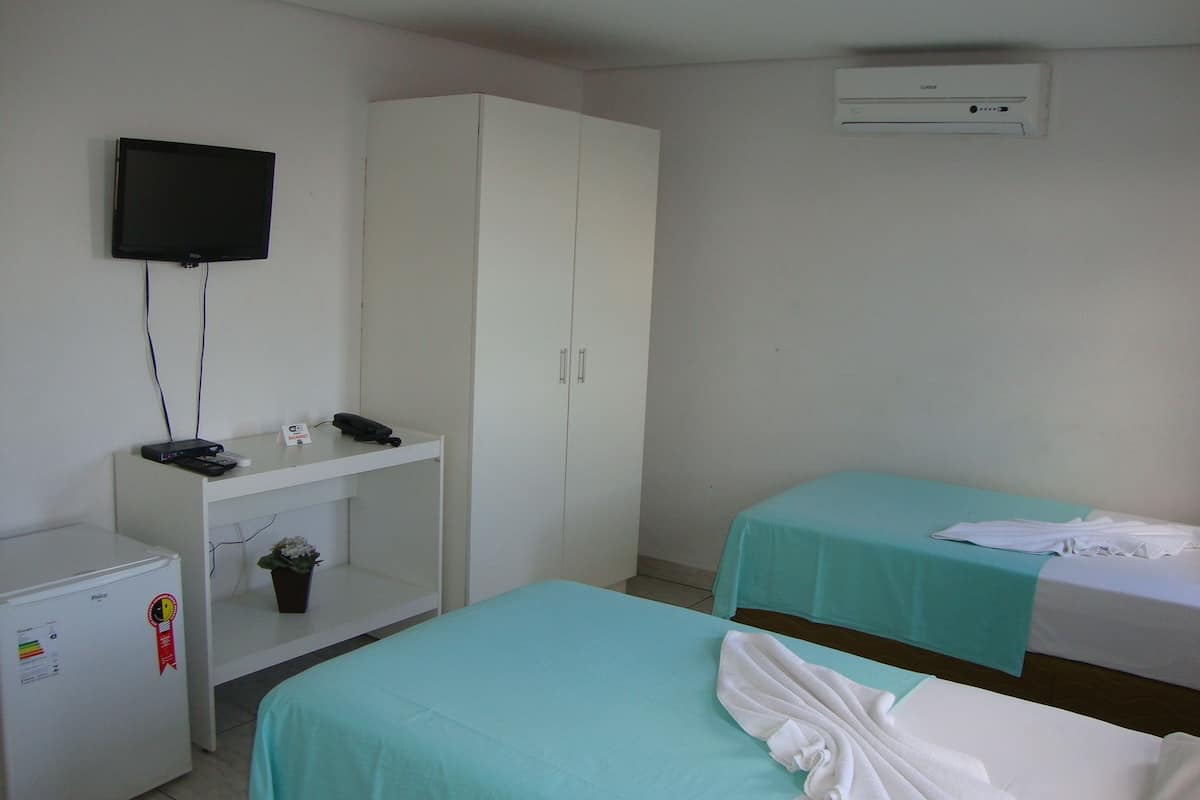 Ein Hotelzimmer mit zwei Betten, einem Fernseher, einem Schreibtisch mit Telefon und einer Klimaanlage.