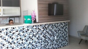 A reception area with a tiled counter, a mounted television, and a signboard. - D'arc Hotel (Goiania)