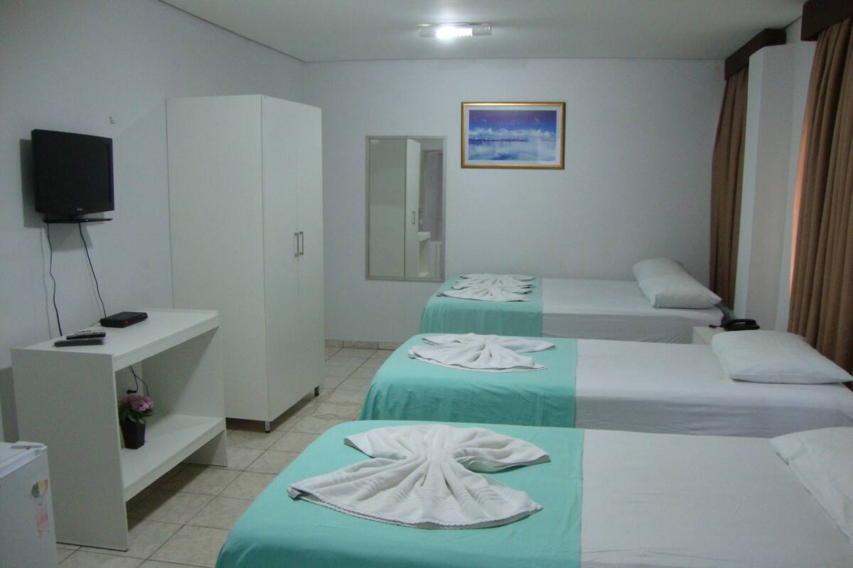 Ein Hotelzimmer mit zwei Betten, einem Fernseher, einem Kleiderschrank und einem Badezimmerspiegel.