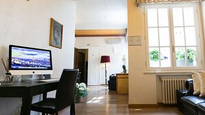 Ett vardagsrum med ett skrivbord, en dator, en soffa och ett fönster med utsikt över grönområden.