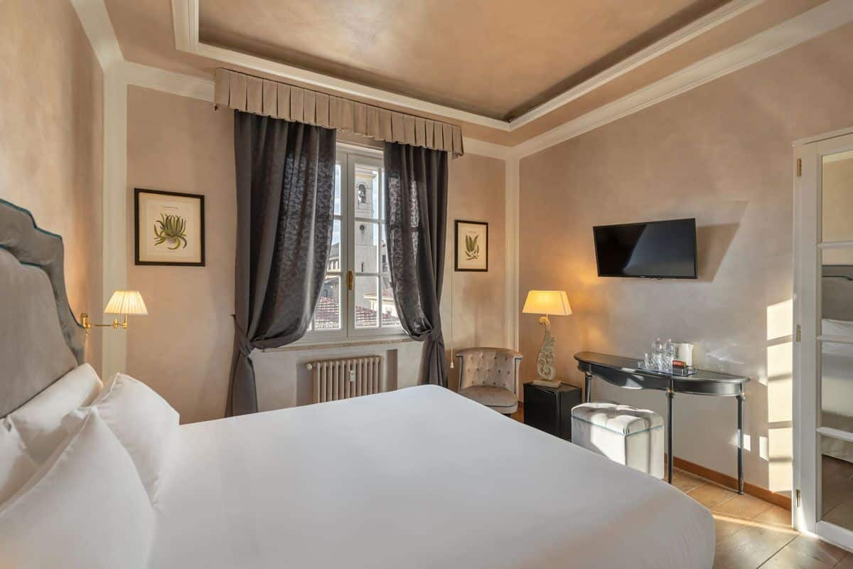A hotel room with a large bed, a desk with a lamp, a chair, and a TV mounted on the wall.