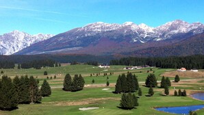 Un parcours de golf avec un étang, entouré d’arbres et avec des montagnes en arrière-plan.
