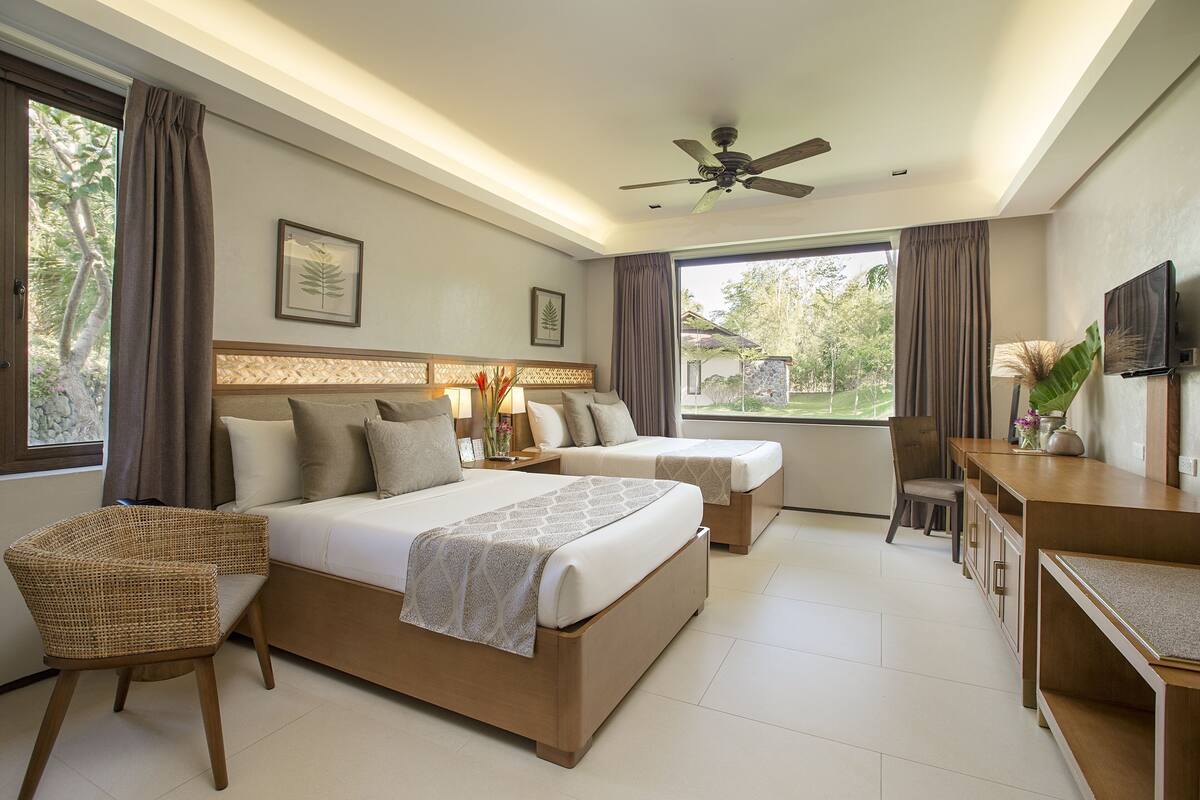 Una habitación de hotel moderna con una cama grande, un escritorio y una silla. Hay un ventilador de techo y un televisor en la pared.