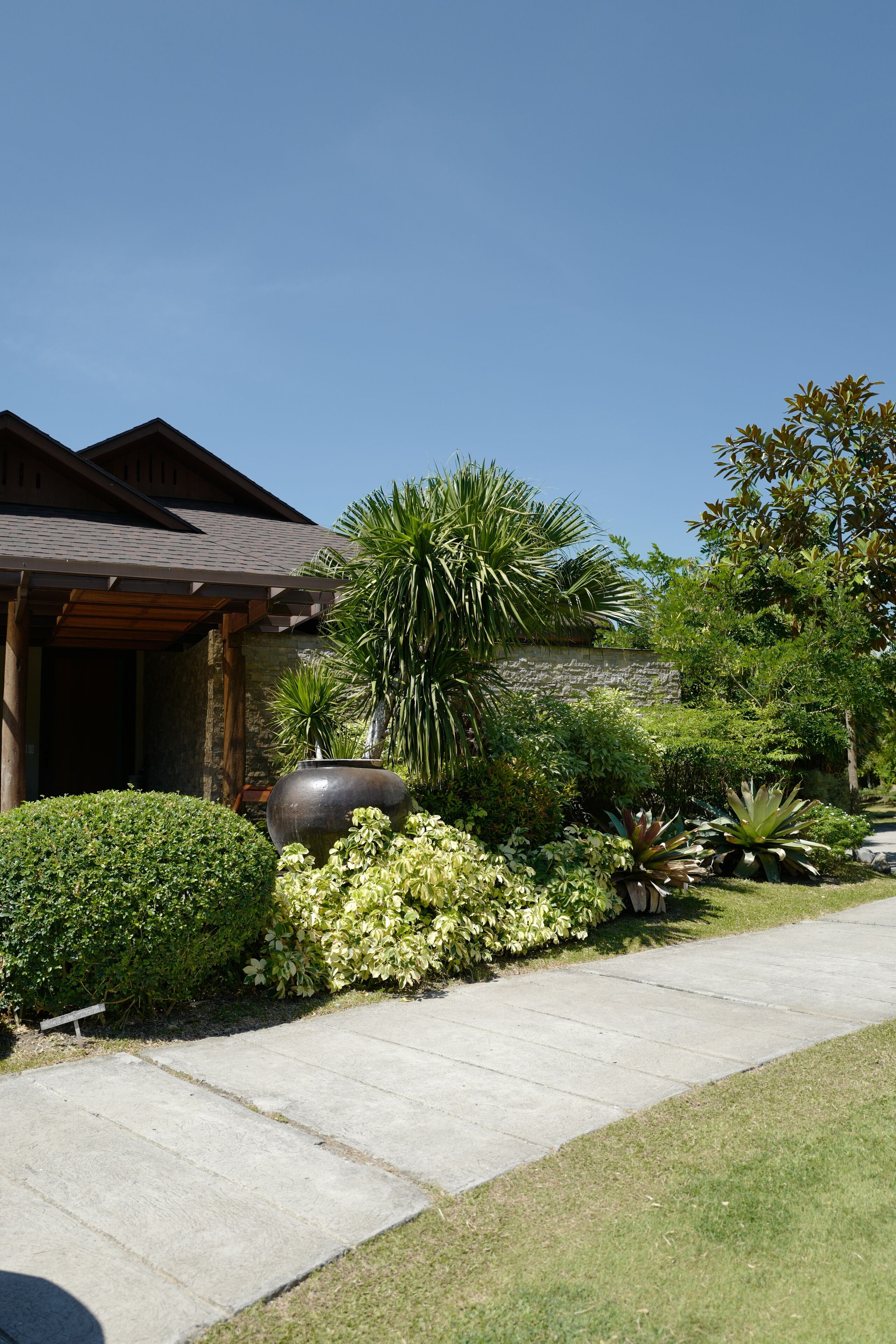 A building with a stone facade, a covered patio, and a well-maintained garden with various plants and a large decorative pot.