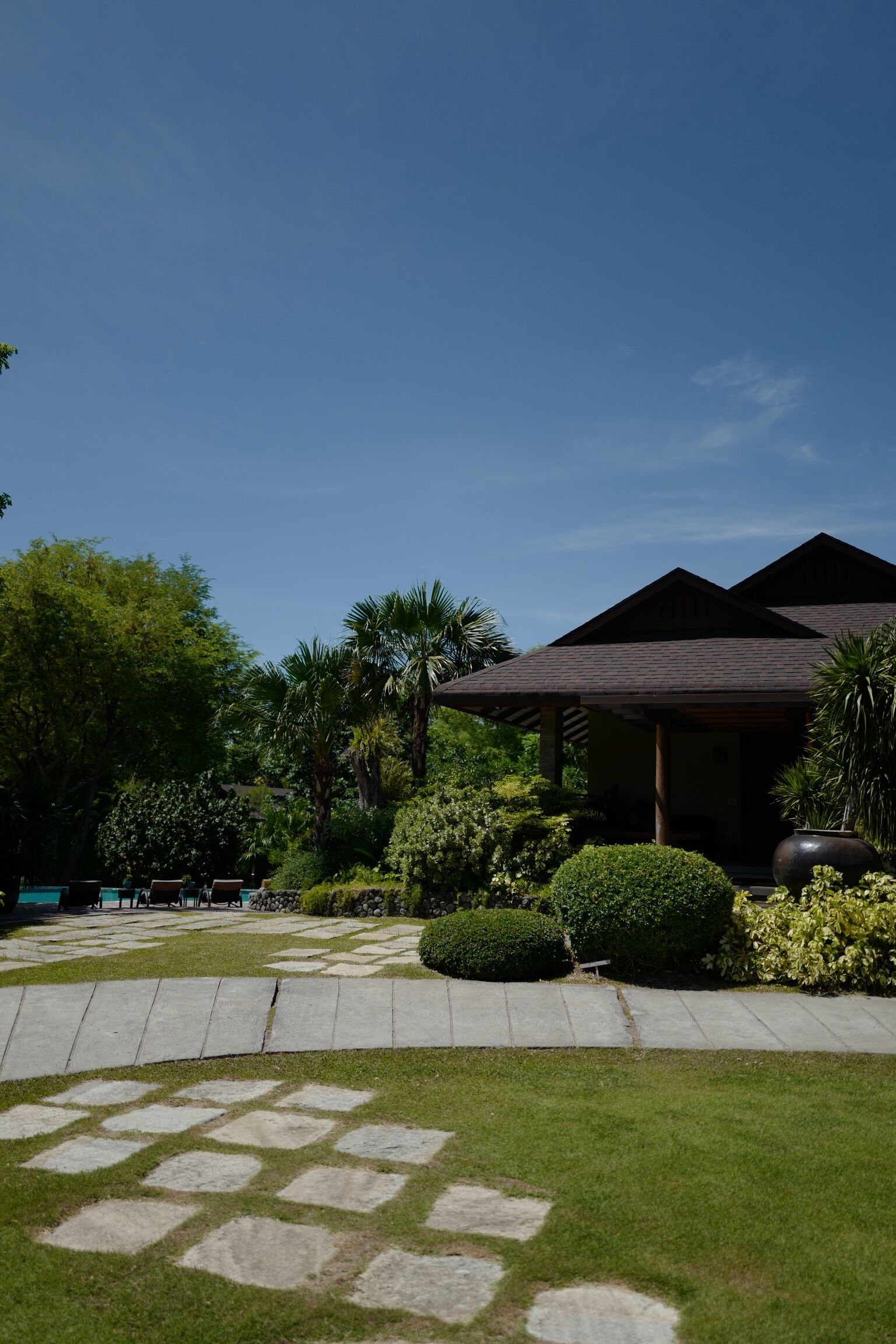 A traditional-style building with a tiled roof, surrounded by lush greenery and a stone pathway.