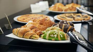 A variety of pastries on display, including croissants and other baked goods, with a serving spoon and a menu card visible.