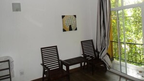 A room with two wooden chairs, a small table, a window with curtains, and a wall-mounted picture. - River edge Bungalow (Rattota)