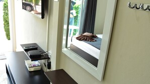 Une chambre d’hôtel moderne dotée d’un téléviseur à écran plat fixé au mur, d’une table de chevet avec une télécommande, d’un petit banc et d’une fenêtre donnant sur un paysage verdoyant.