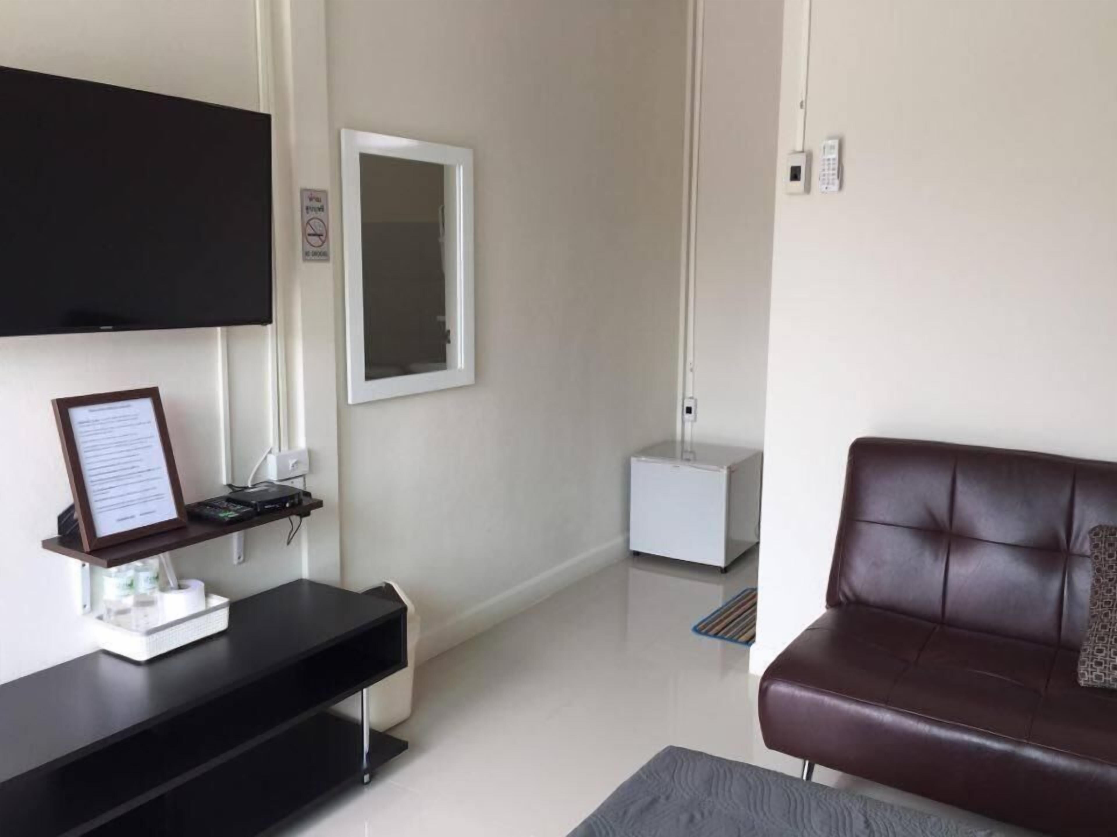 Una sala de estar moderna con un televisor de pantalla plana montado en la pared, un sofá de cuero marrón oscuro, una mesita auxiliar blanca con un diploma enmarcado, y un mueble blanco pequeño.