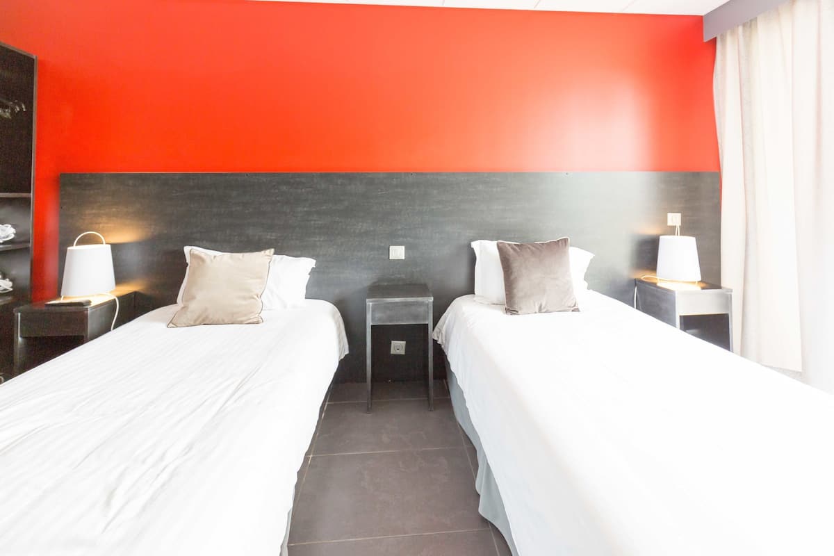 Una habitación de hotel con dos camas, una mesita de noche con lámpara y una pequeña mesa.