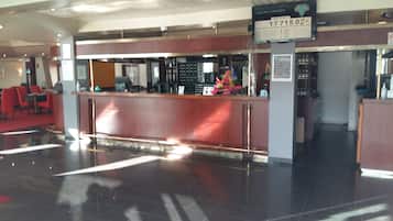A reception desk with a sign displaying room rates, a seating area with red chairs, and a tiled floor.