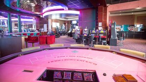 Ein Casino-Bereich mit Spieltischen, Stühlen und Spielautomaten.