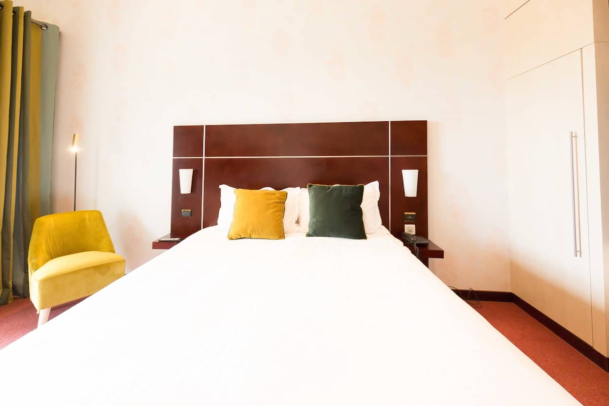 Habitación de hotel con una cama grande, dos mesitas de noche, un tocador, una silla y un armario.