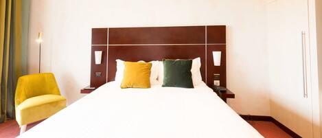 Habitación de hotel con una cama grande, dos mesitas de noche, un tocador, una silla y un armario.