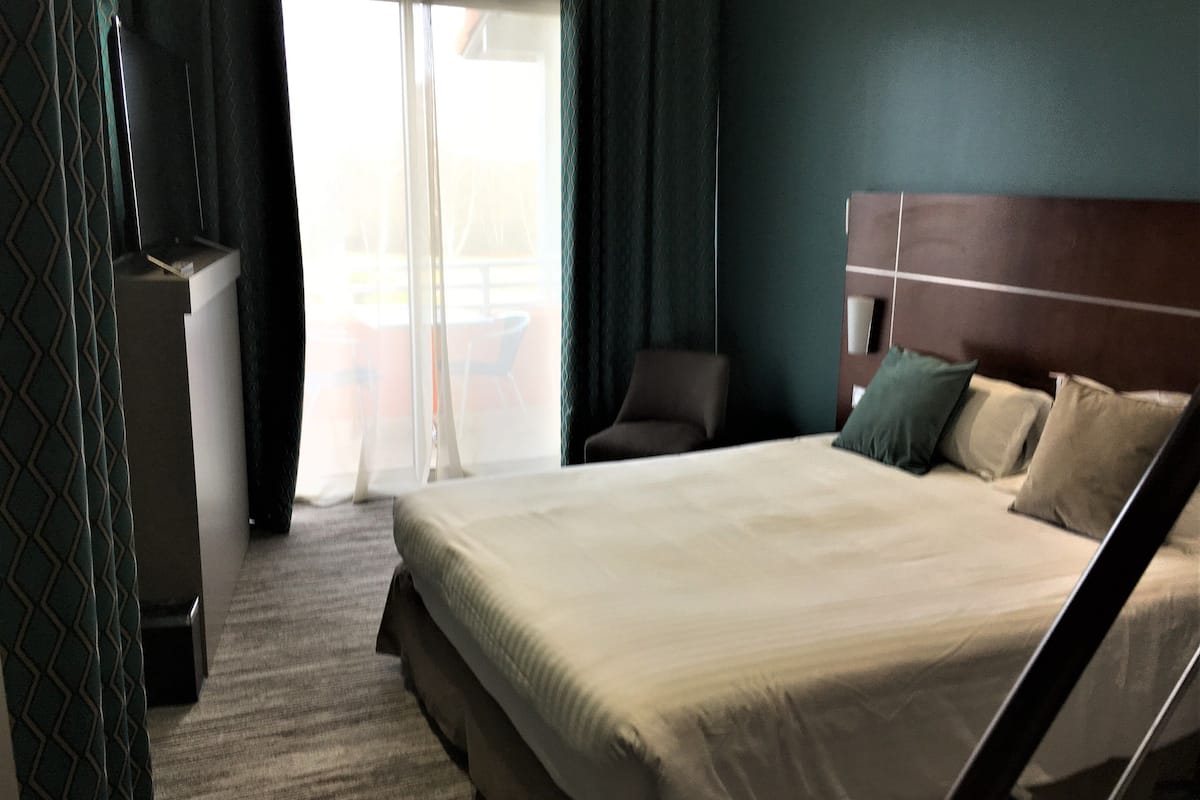 Habitación de hotel con cama, una silla, un escritorio y vistas al exterior.