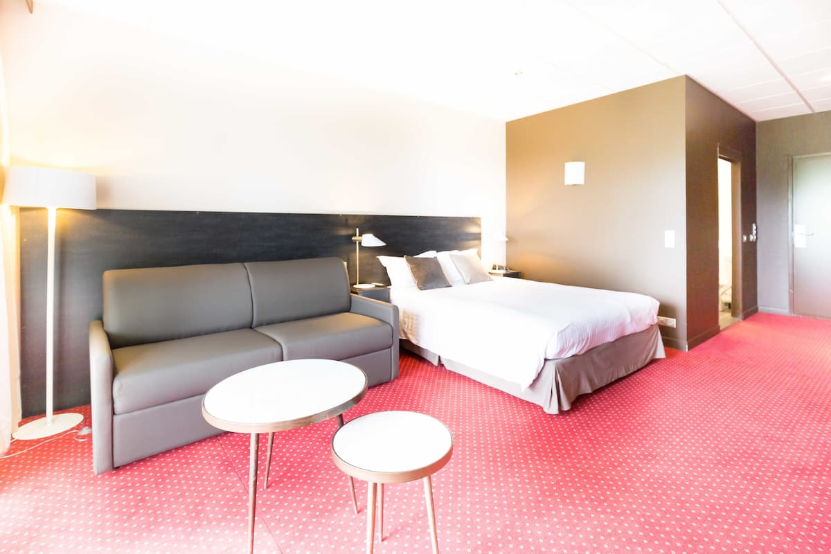 Habitaci ón de hotel con un sofá gris, una cama con ropa de cama blanca, dos mesitas de noche y una alfombra roja.