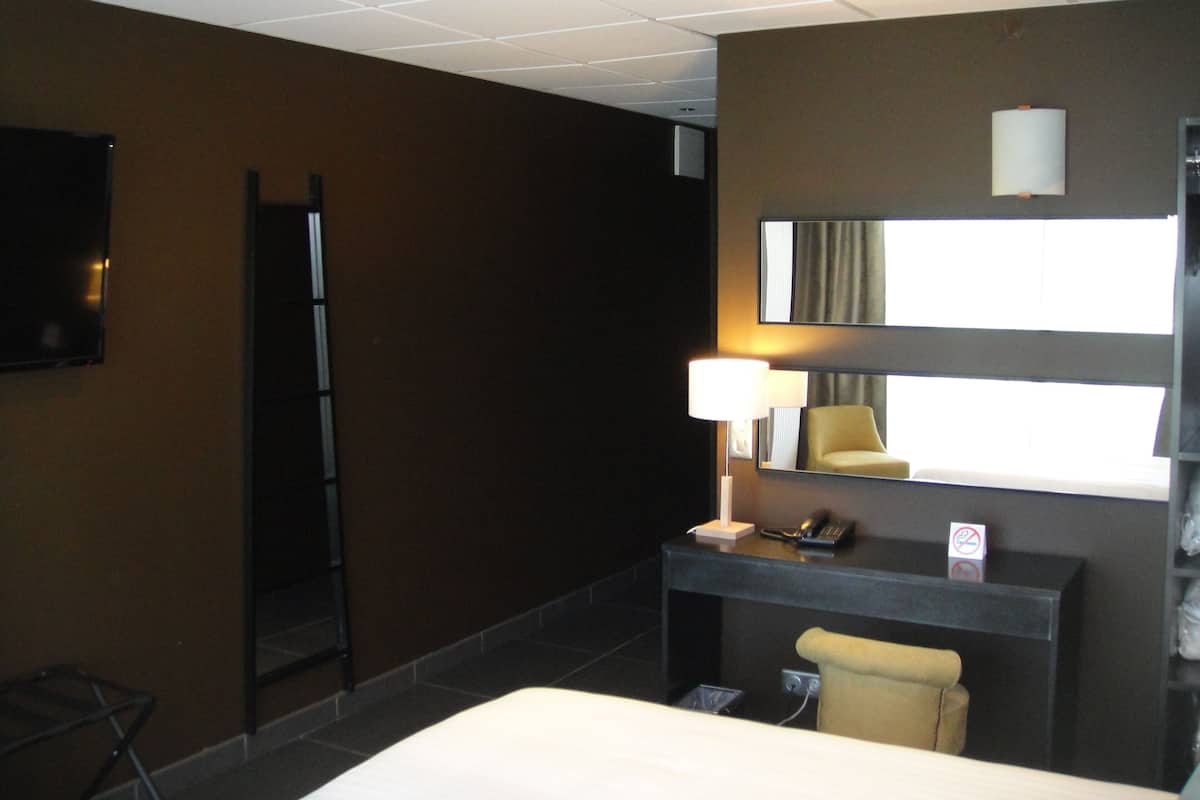 Una habitación de hotel con una cama, un escritorio con lámpara, un teléfono y un espejo.