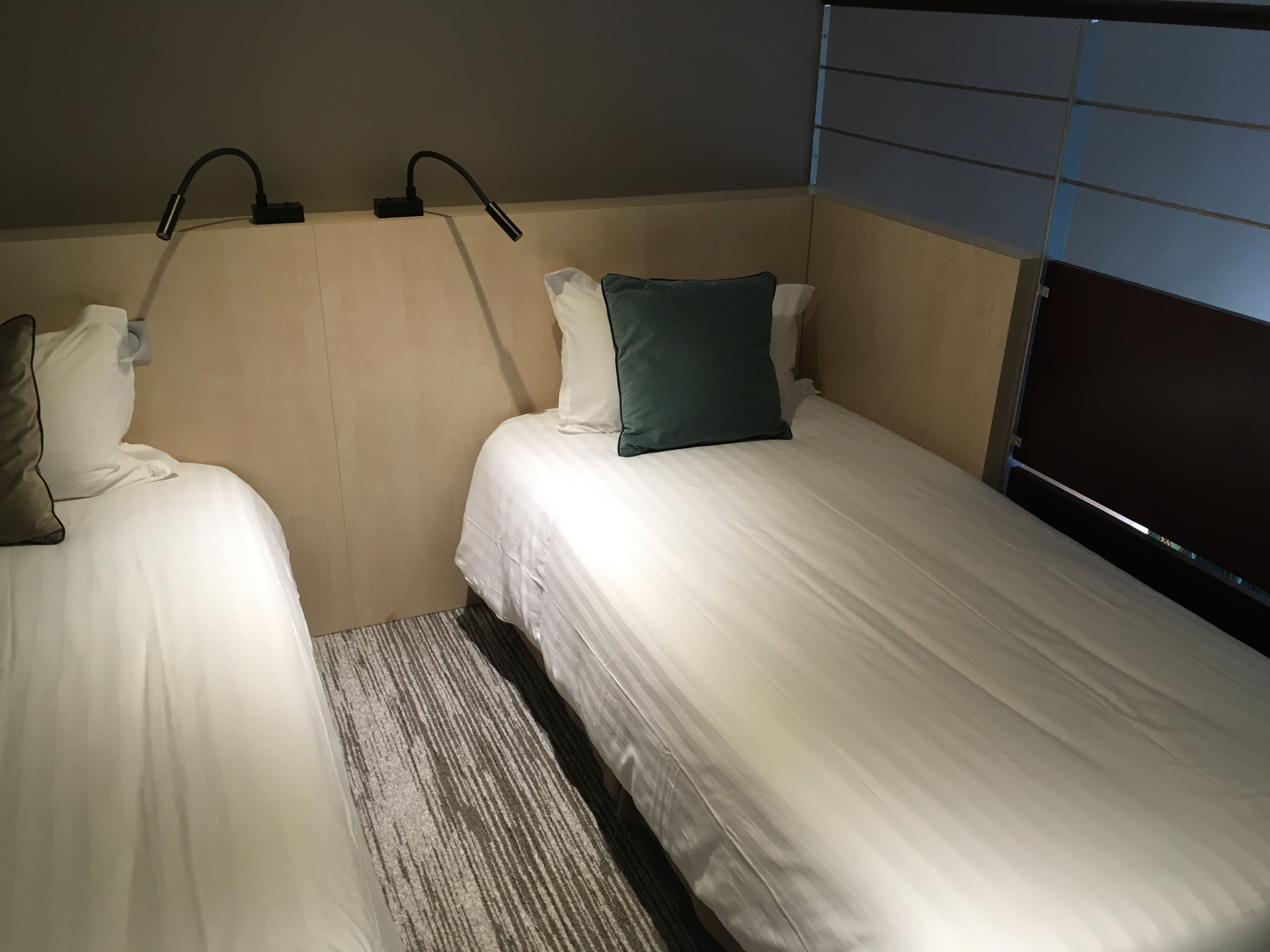 Habitación de hotel con dos camas individuales, cabecera con lámpara y ventana con persianas.