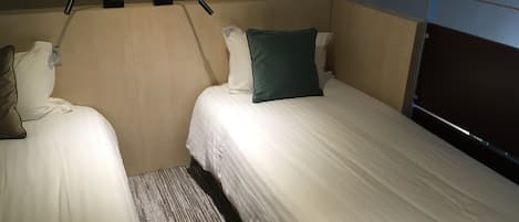 A hotel room with two single beds, a headboard with a light fixture, and a window with blinds.