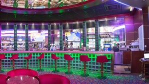 Eine Bar mit einer Theke, mehreren Bildschirmen und roten Barhocker.
