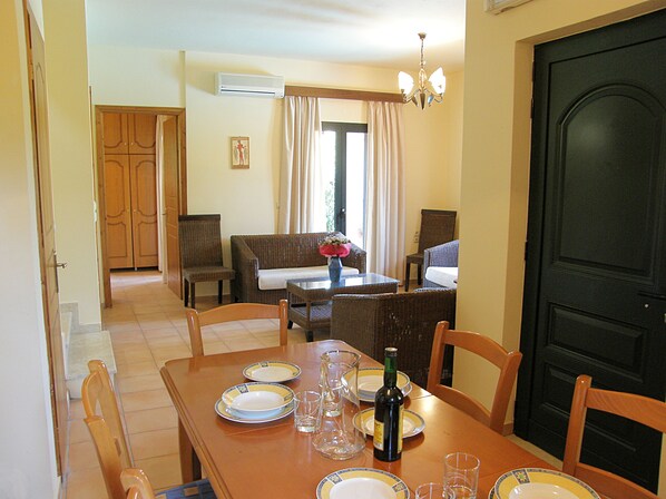 Un comedor con una mesa de madera dispuesta para cuatro personas, sillas, un sofá y una araña.