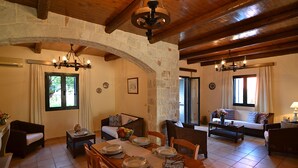 A spacious living area with a stone archway, wooden ceiling beams, and a dining table set for four. - Christina Villas (Heraklion)