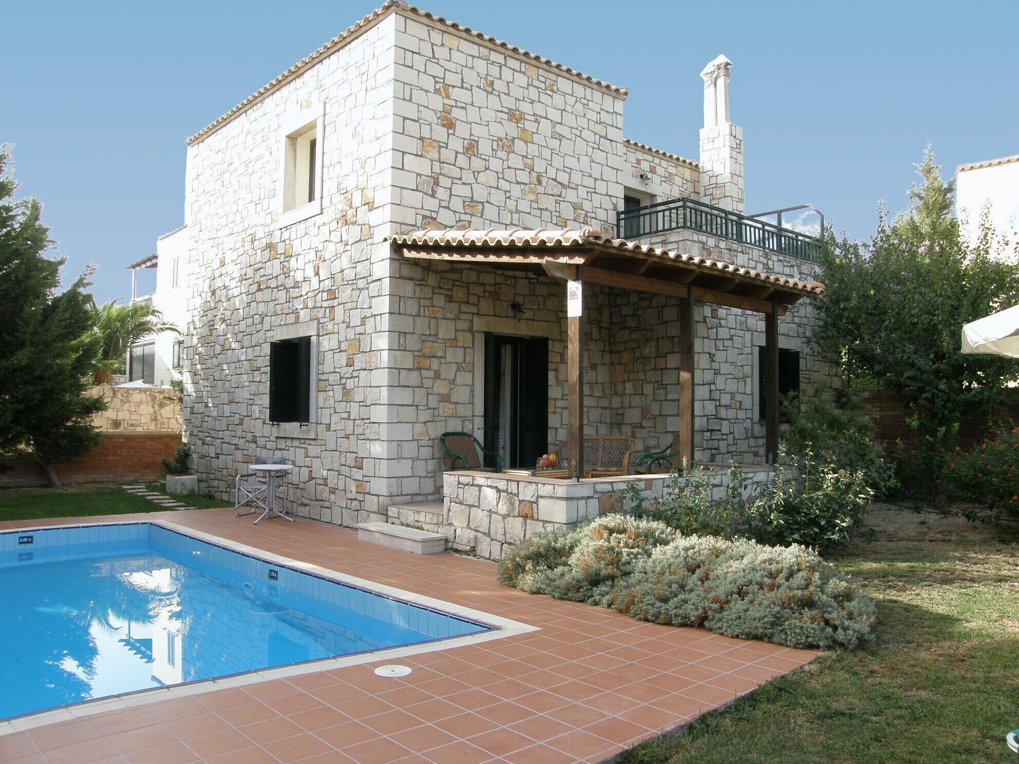 A stone house with a swimming pool, a balcony, and a garden.