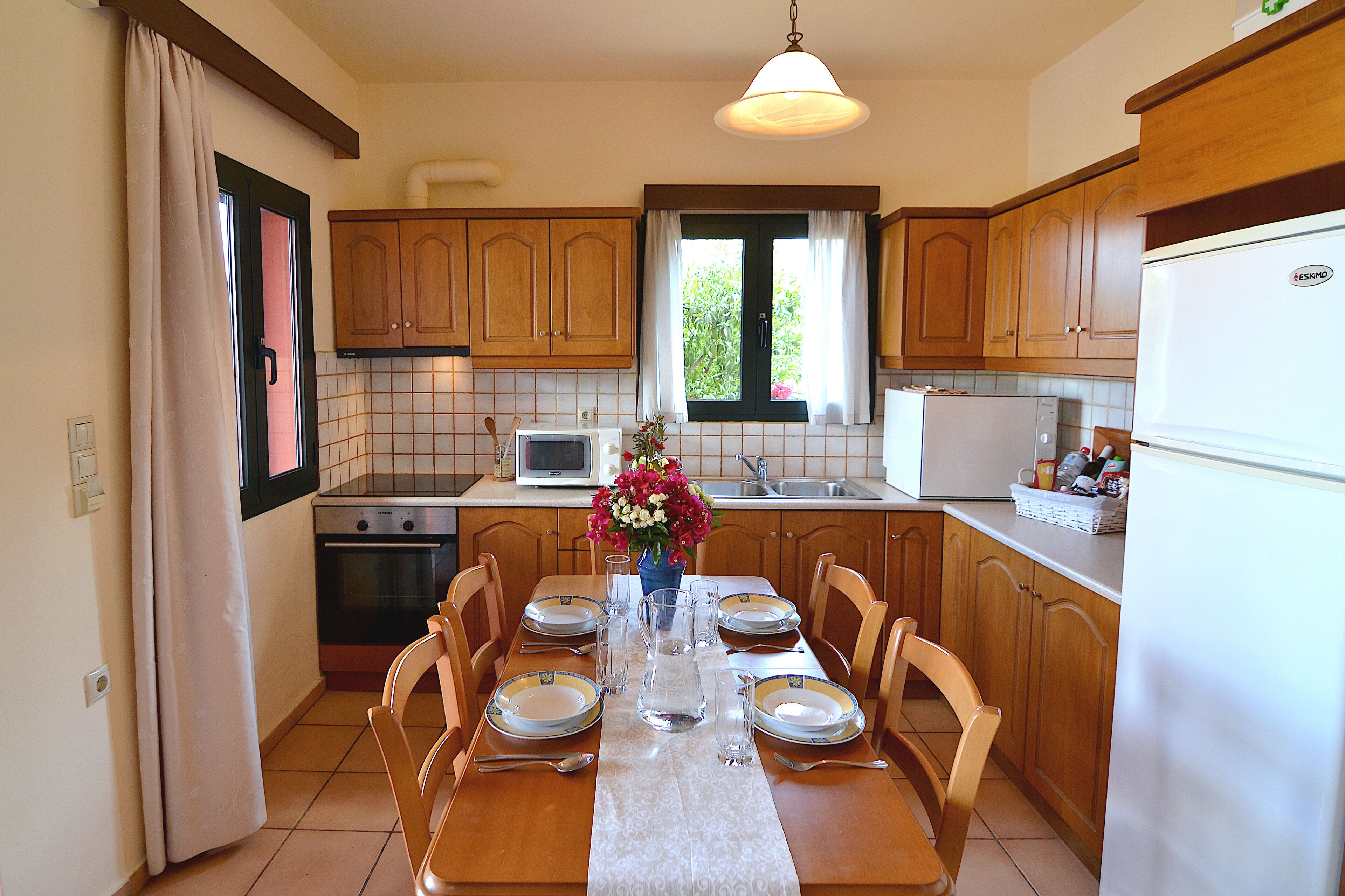 A kitchen with wooden cabinets, a dining table set for four, a microwave, and a refrigerator.