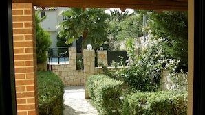 A stone pathway leading through a garden area with a brick wall on one side and a wooden pergola overhead. - Christina Villas (Heraklion)