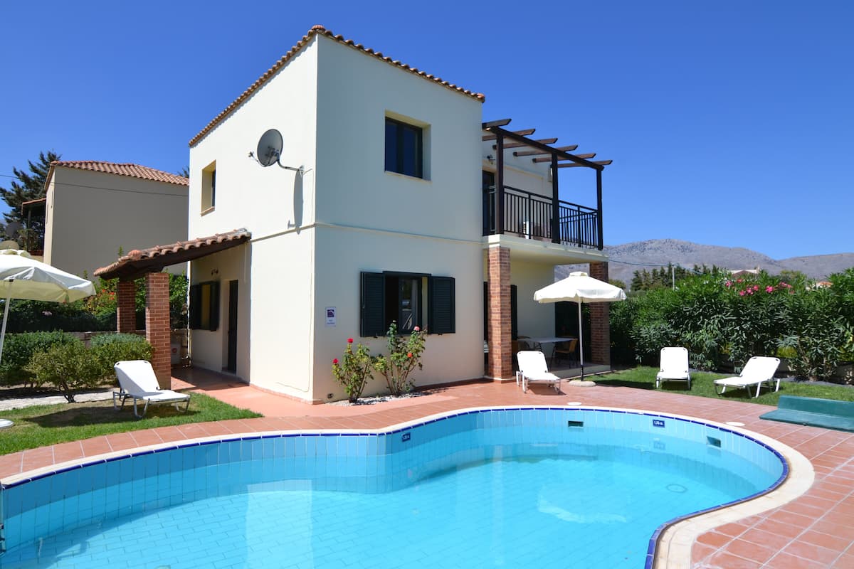 A two-story house with a swimming pool, a balcony, and a patio area with lounge chairs.