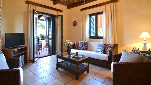 A living room with a television, sofa, coffee table, and a dining area visible through an open door. - Christina Villas (Heraklion)