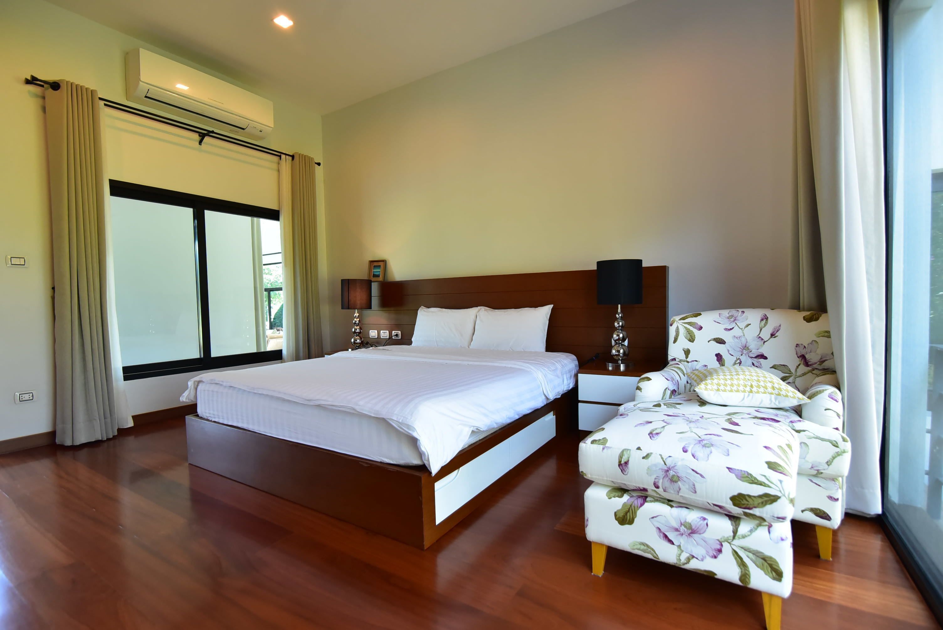 Quarto de hotel com uma cama grande, uma cadeira com estofamento floral e uma janela com cortinas.