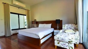 Quarto de hotel com uma cama grande, uma cadeira com estofamento floral e uma janela com cortinas.