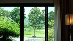 Habitación de hotel con un ventanal grande que ofrece vistas de un paisaje verde exuberante con árboles y una masa de agua.