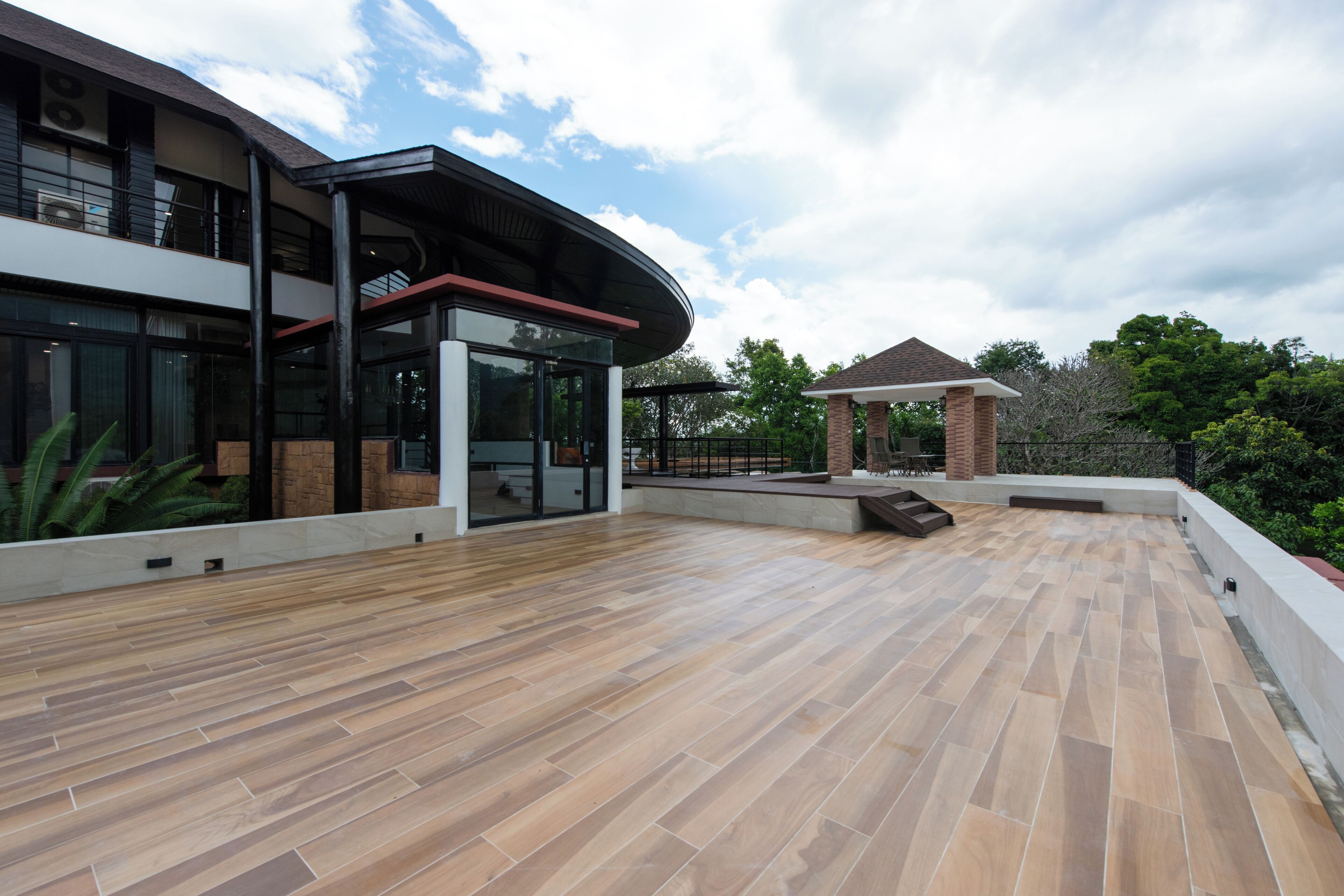 A spacious outdoor area with a wooden deck, a covered seating area, and a modern building with large windows and a brick structure.