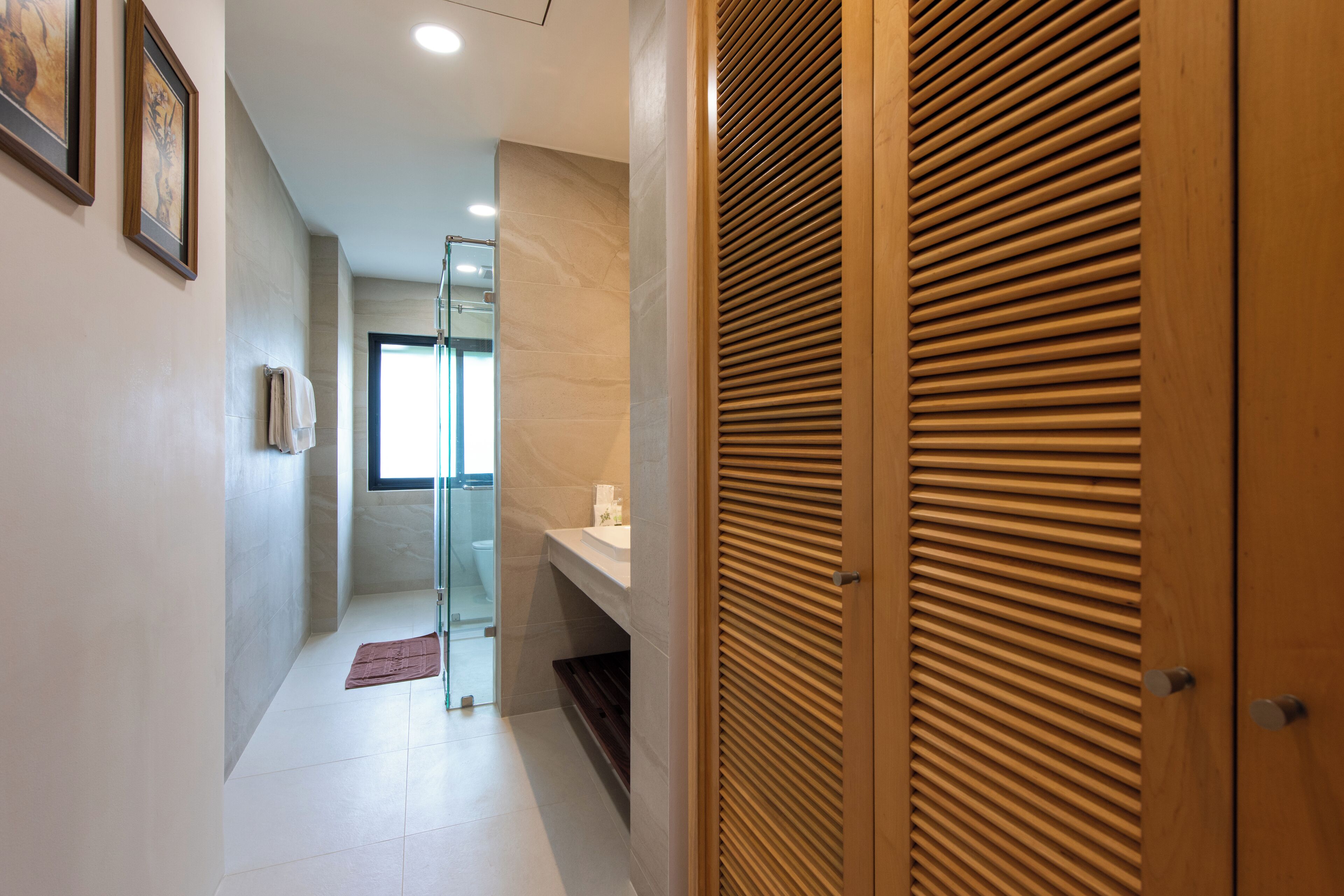 A hallway with a wooden door, a glass shower enclosure, and a white tiled floor.