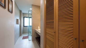 A hallway with a wooden door, a glass shower enclosure, and a white tiled floor.