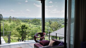 Una sala de estar moderna con un gran ventanal que da a un balcón con vistas a un paisaje verde exuberante.