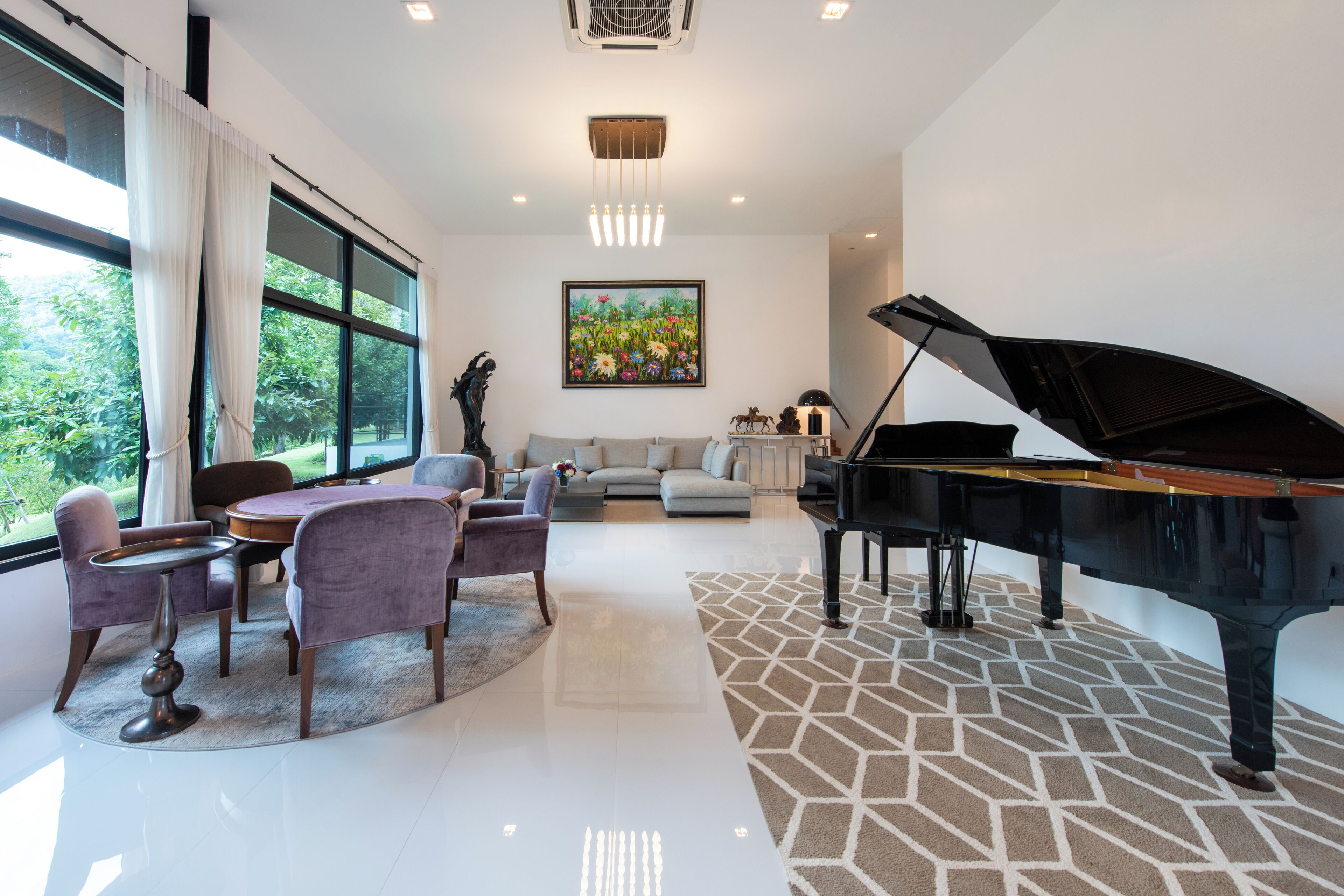 A modern living room with a grand piano, a dining area with a round table, and a large window offering a view of greenery.