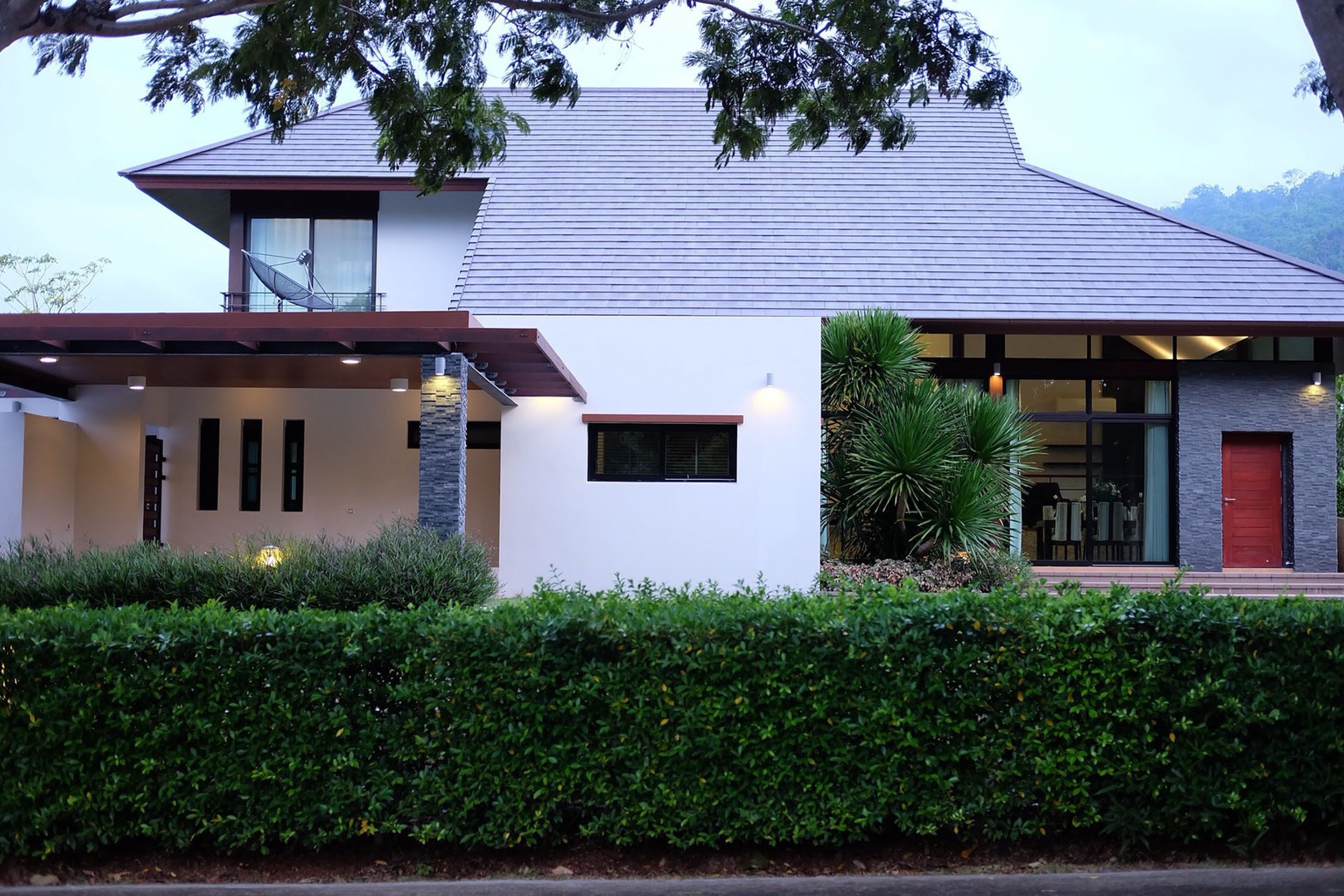 A modern two-story house with a sloped roof, large windows, and a well-maintained hedge in front.