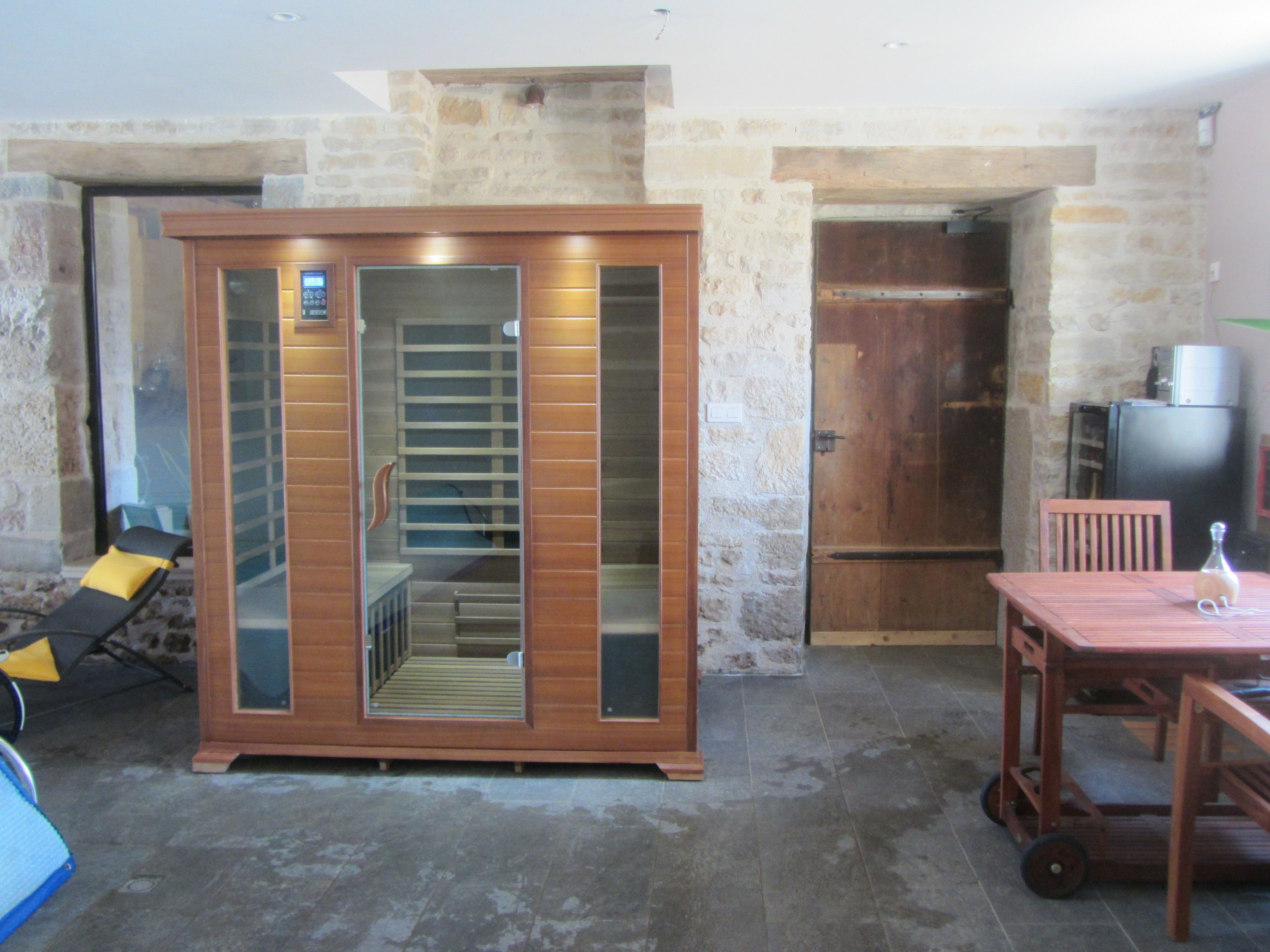 Una habitación con una puerta de vidrio corredera que da a una escalera, una mesa de madera con una botella y un refrigerador negro.