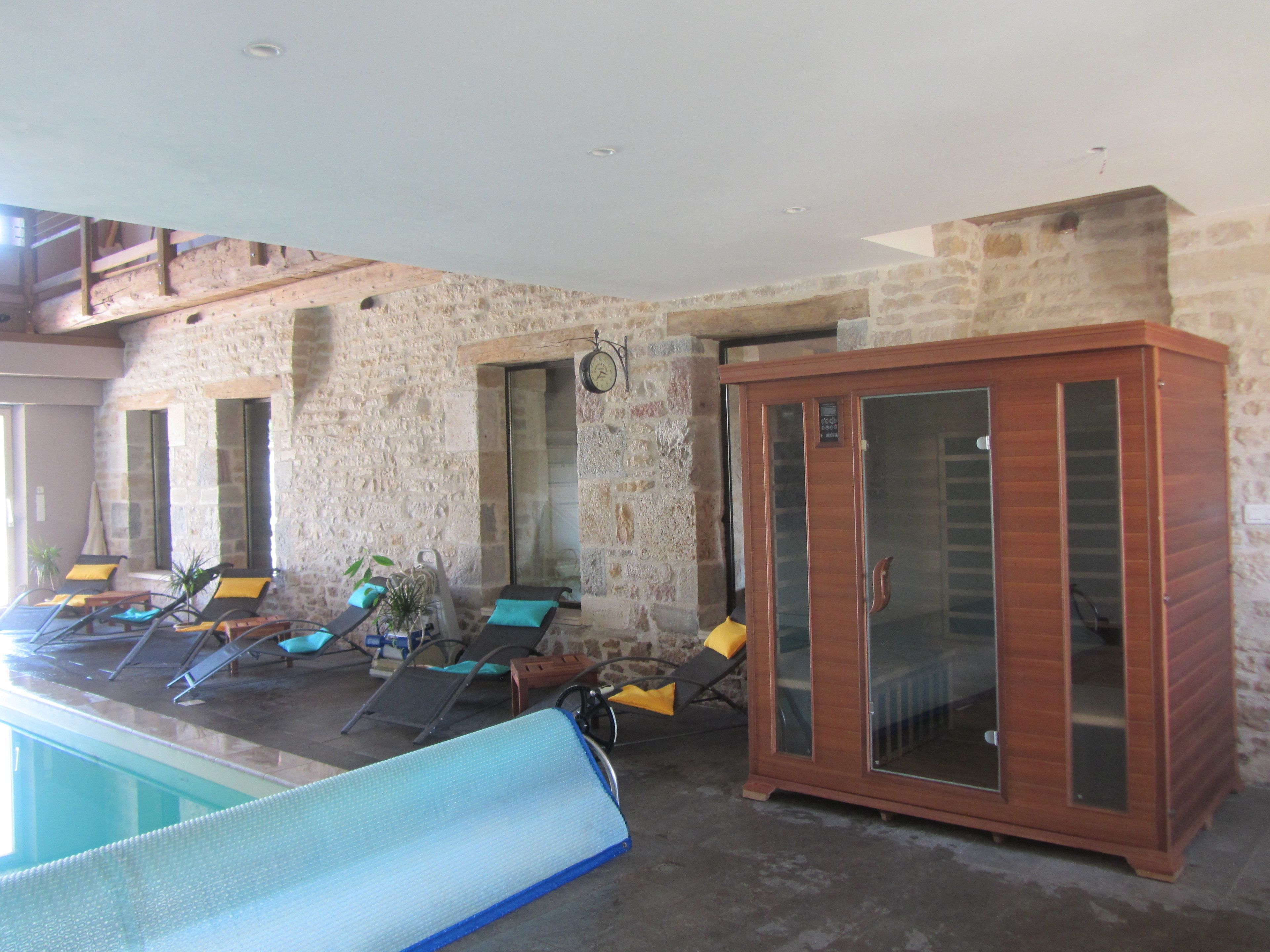 Une pièce aux murs de pierre, dotée d’une piscine, de chaises longues et d’un meuble de rangement.