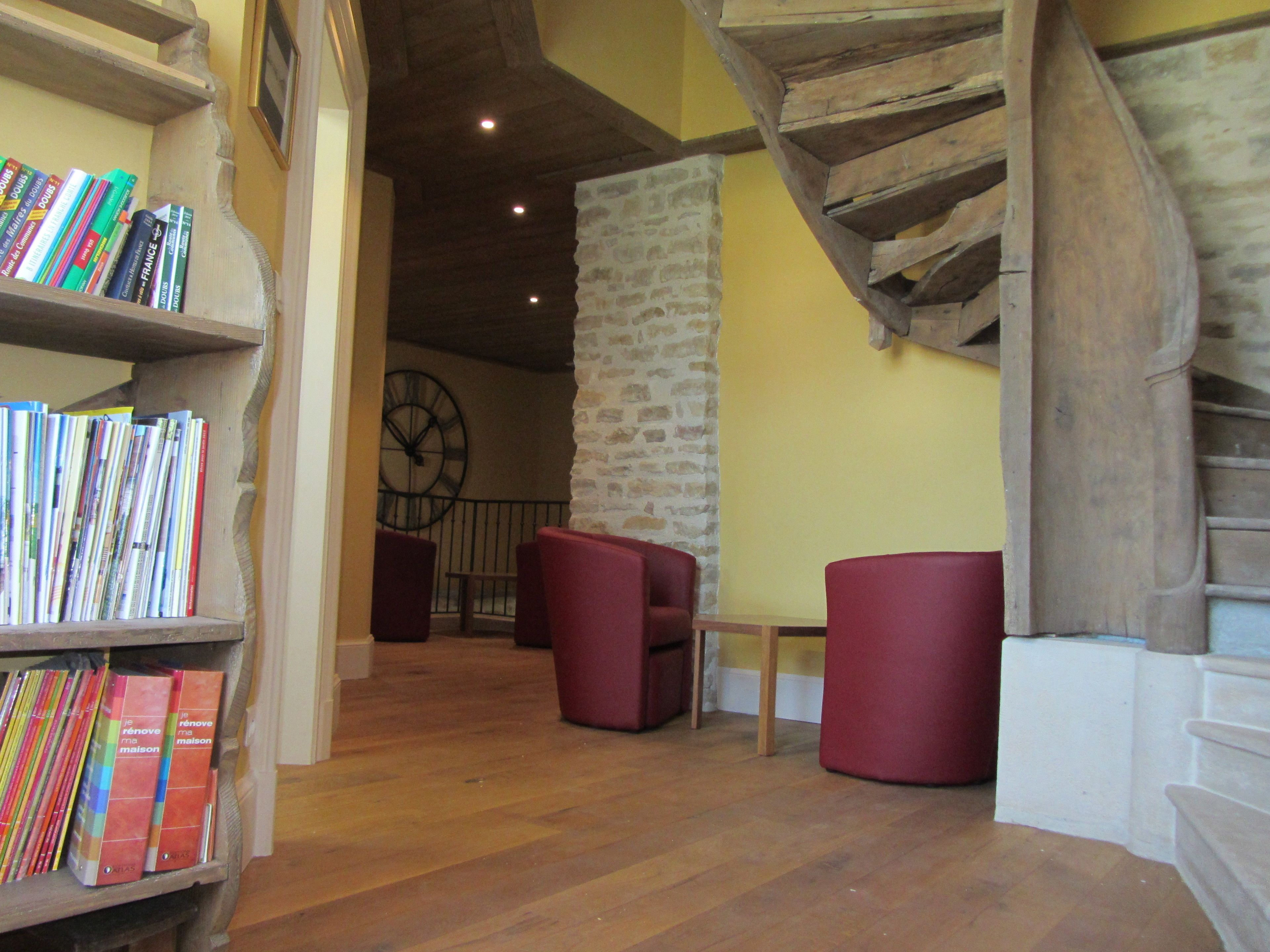 A cozy interior with a wooden staircase, a stone wall, and a bookshelf filled with books.