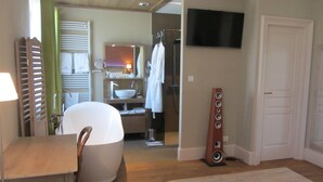 A hotel room with a large bed, a wooden dining table, a TV mounted on the wall, and a bathroom with a sink and mirror. - Le Relais des Deux Tours (Bremondans)