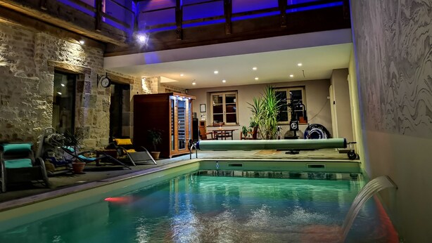 An indoor swimming pool with a stone wall, lounge chairs, and a ceiling with blue lighting. - Le Relais des Deux Tours (Bremondans)